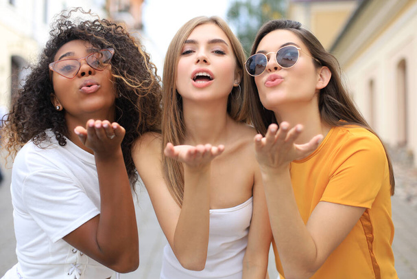 Drei junge lächelnde Hipster-Frauen in Sommerkleidung posieren auf der Straße. Weibchen zeigen positive Gefühle. - Foto, Bild