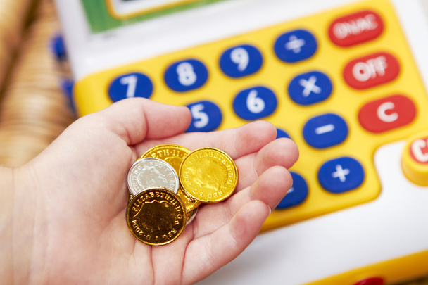 Child's Hand Holding Pretend Coins Next To Toy Cash Register - Фото, изображение