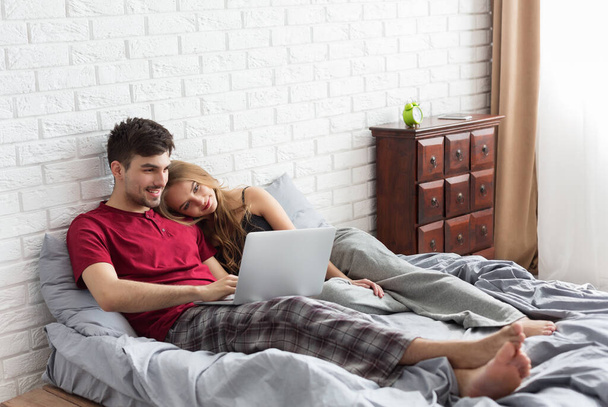 "Fiatal házaspár fekszik az ágyon és laptopot használ" - Fotó, kép