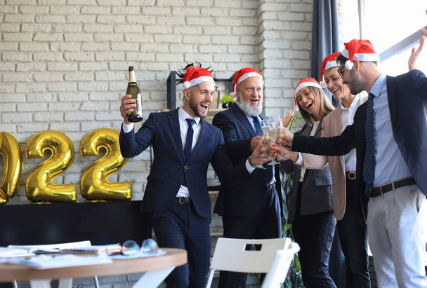 Zakenmensen vieren vakantie in modern kantoor met champagne drinken en plezier hebben in samenwerken. Vrolijk Kerstfeest en Gelukkig Nieuwjaar 2022. - Foto, afbeelding