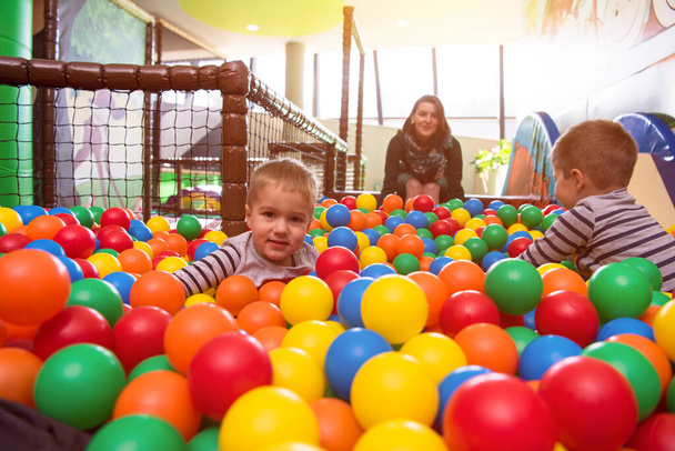 jong mam spelen met kinderen in zwembad met kleurrijke ballen - Foto, afbeelding