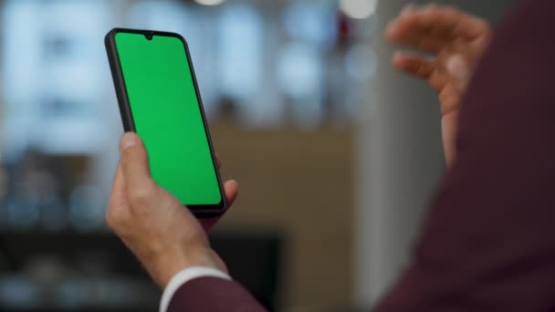 Closeup unknown man greeting chromakey smartphone at office. Unrecognizable boss using mockup mobile device indoor. Employee director waving hand to green screen during video call at open space  - Footage, Video