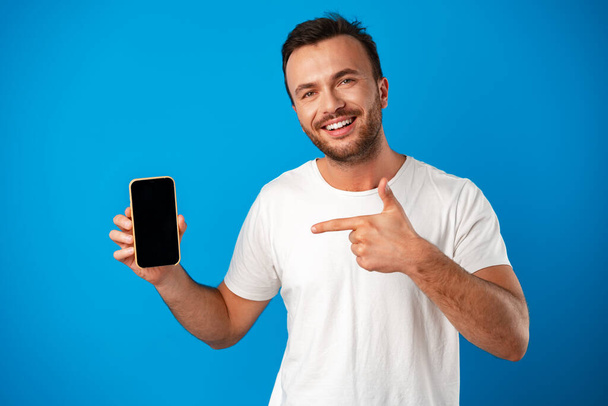 "Ritratto di giovane uomo pubblicità nuovo smartphone, mostrandolo alla fotocamera sullo sfondo blu" - Foto, immagini