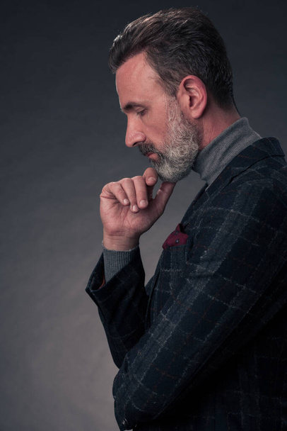 Портрет стильного элегантного старшего бизнесмена с бородой и повседневной деловой одеждой в фотостудии, изолированной на темном фоне жестом руками - Фото, изображение