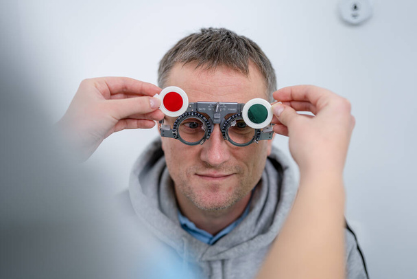 "Un patient de sexe masculin subit un test oculaire et une prescription de lunettes dans une clinique d'ophtalmologie. Optométriste vérifiant la vue du patient et la correction de la vue. Changement de lentilles sur le cadre de l'essai sur le nez du patient" - Photo, image