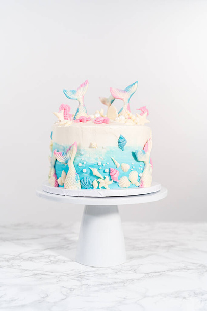 Zeemeermin-thema 3 lagen vanille taart versierd met chocolade zeemeermin staarten en schelpen op een witte taart staan. - Foto, afbeelding