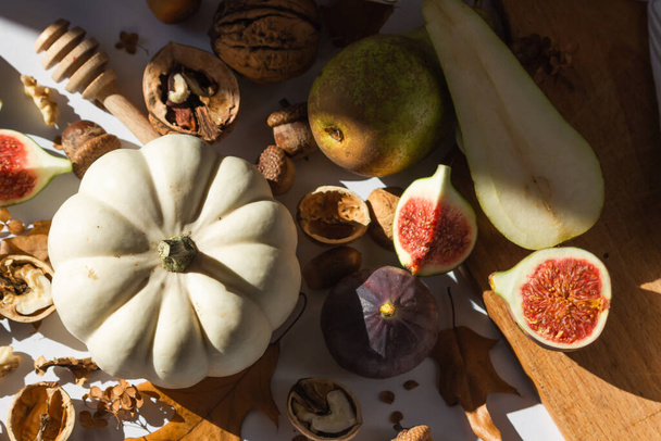 Autumn still-life with white pumpkin, sliced figs, walnuts and pears on wooden cutting board. Decorated by dry oak leaves and acorns. Ingredients for autumn recipes. Healthy eating concept. Top view. - Zdjęcie, obraz