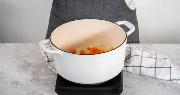 Sauteing λαχανικά σε σμάλτο χυτοσίδηρο ολλανδικό φούρνο για να μαγειρέψουν σούπα μπιζελιού διάσπαση. - Φωτογραφία, εικόνα