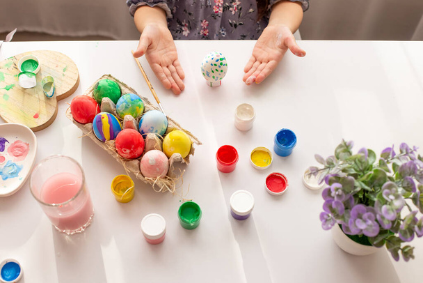 "De handen van een klein meisje, palmen omhoog, demonstreren een beschilderd ei, op een witte tafel met veelkleurige eieren" - Foto, afbeelding