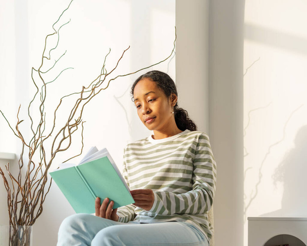 "Afro-Amerikaanse vrouw die vredig boek leest in de lounge. Genieten van het moment. Langzame levensstijl" - Foto, afbeelding