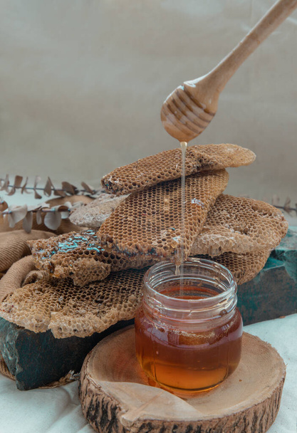 "Delicious honey dripping from Wooden honey dipper stick into on Glass jar and Fresh honeycombs background. " - Photo, Image