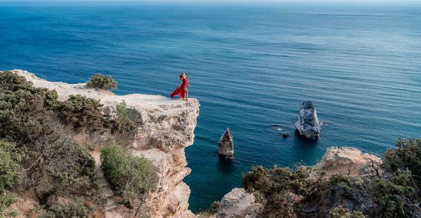 Kobieta w czerwonej latającej sukience trzepocze na wietrze, na tle morza. - Zdjęcie, obraz