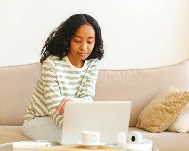 "Αφρο-αμερικανίδα γυναίκα κάθεται στον καναπέ και χρησιμοποιεί ψηφιακή συσκευή για εργασία και μελέτη" - Φωτογραφία, εικόνα