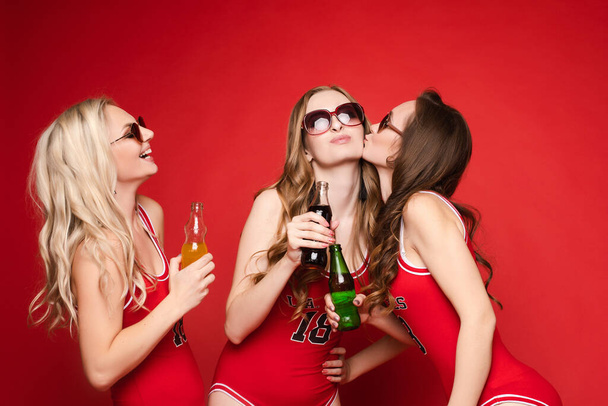 "Gyönyörű és boldog női barátok élénk piros fürdőruhában, hideg italokkal a kezükben, vörös alapon, stúdió." - Fotó, kép