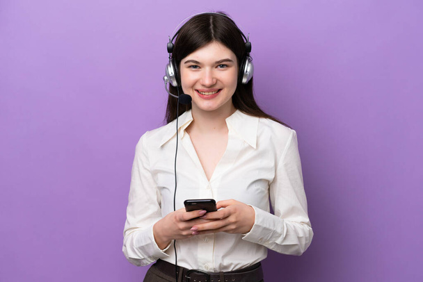 Telemarketer Orosz nő dolgozik egy headset elszigetelt lila háttér küld egy üzenetet a mobil - Fotó, kép