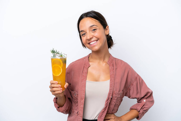 Young hispanic woman holding a cocktail isolated on white background posing with arms at hip and smiling - Fotografie, Obrázek