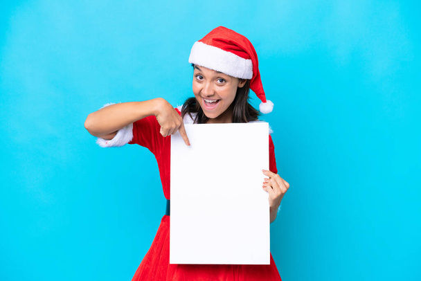 Anne Noel gibi giyinmiş genç İspanyol kadın beyaz arka planda izole edilmiş, elinde mutlu bir ifadeyle boş bir levha tutuyor ve onu işaret ediyor. - Fotoğraf, Görsel
