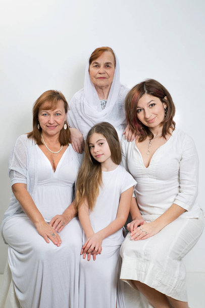 Groepsportret van vrouwen van dezelfde familie van verschillende generaties in lichte kleren op een witte achtergrond. - Foto, afbeelding