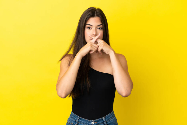 Young Brazilian woman isolated on yellow background showing a sign of silence gesture - Valokuva, kuva