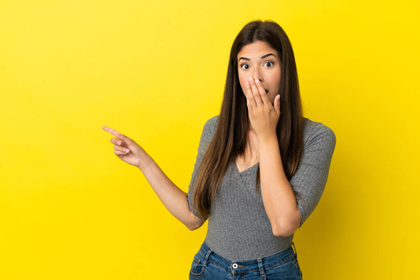 Young Brazilian woman isolated on yellow background with surprise expression while pointing side - Fotografie, Obrázek