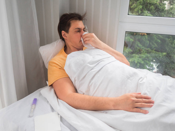 "El enfermo está acostado en la cama con el termómetro. El hombre se está sonando la nariz. Incapacidad temporal en caso de síntomas de enfermedad." - Foto, imagen