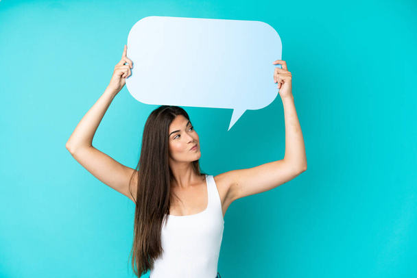 Young Brazilian woman isolated on blue background holding an empty speech bubble and with sad expression - Photo, Image