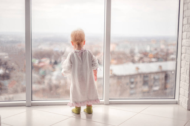"bambina con un vestito carino guarda fuori dalla finestra" - Foto, immagini
