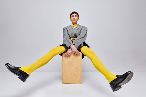 Muotokuva tyylikäs poika poseeraa takki, bleiseri ja keltainen sukkahousut eristetty harmaalla pohjalla. Outo teini-ikäinen. Käsitteen moderni muoti, taide valokuvaus, tyyli, queer, ainutlaatuisuus, mainos - Valokuva, kuva
