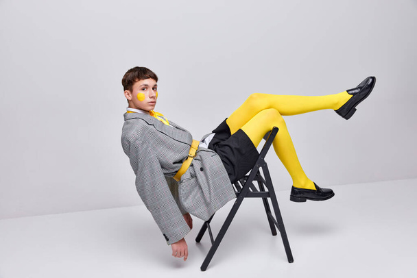 Portrait of stylish boy posing in jacket, blazer and yellow tights isolated over grey background. Bright teen fashion. Concept of modern fashion, art photography, style, queer, uniqueness, ad - Фото, зображення