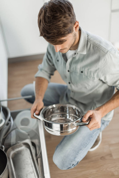 "jeune homme regardant la vaisselle propre au lave-vaisselle" - Photo, image
