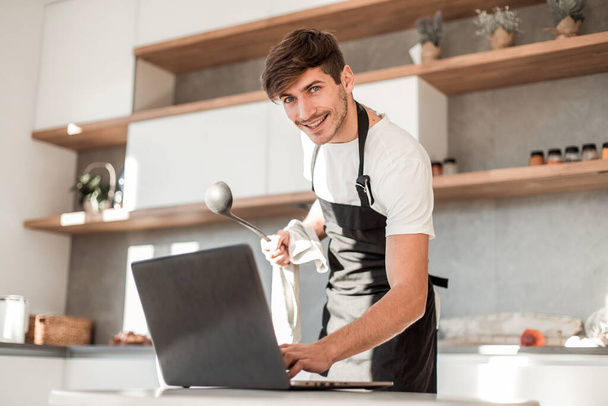 "Genç adam yemek pişirirken dizüstü bilgisayara bakıyor." - Fotoğraf, Görsel