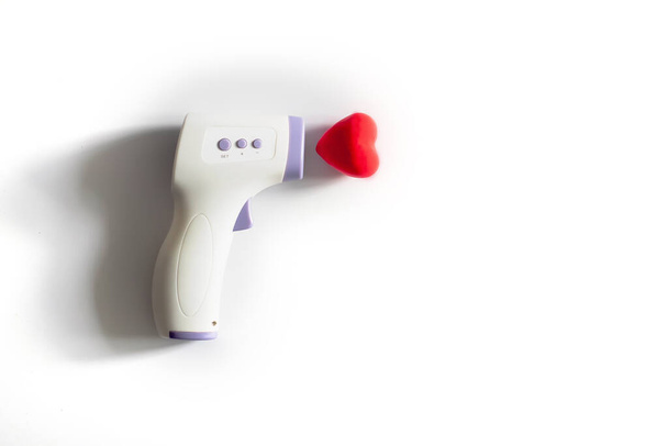 infrared contactless thermometer next to voluminous heart on white background with trend shadows. Heart disease. Measuring temperature. Health concept. - Foto, Imagen