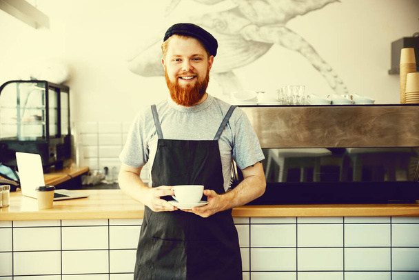 "Właściciel firmy kawa koncepcja - portret szczęśliwy młody Brodaty kaukaski barista w fartuch z pewnie patrząc i uśmiecha się do kamery w kawiarni licznika." - Zdjęcie, obraz