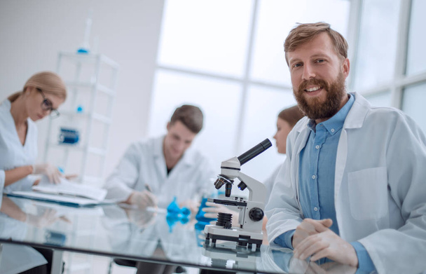 exitoso joven científico sentado en su escritorio en el laboratorio - Foto, imagen