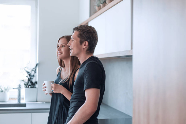 счастливая молодая пара, стоящая на кухне в своем доме. - Фото, изображение