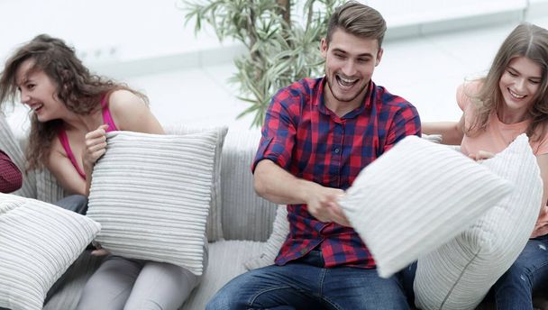 cheerful friends playing pillow fight, sitting on the couch - Fotografie, Obrázek