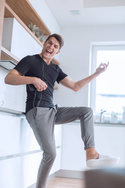 happy young man with smartphone sings in his kitchen - Photo, Image