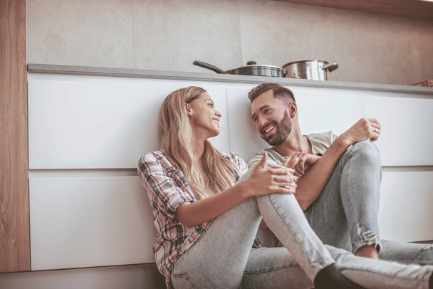 любящая пара обсуждает что-то сидя на полу кухни - Фото, изображение