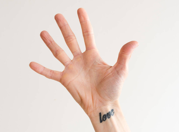 Women's open hand with fingers outstretched and love tattoo on wrist - 写真・画像