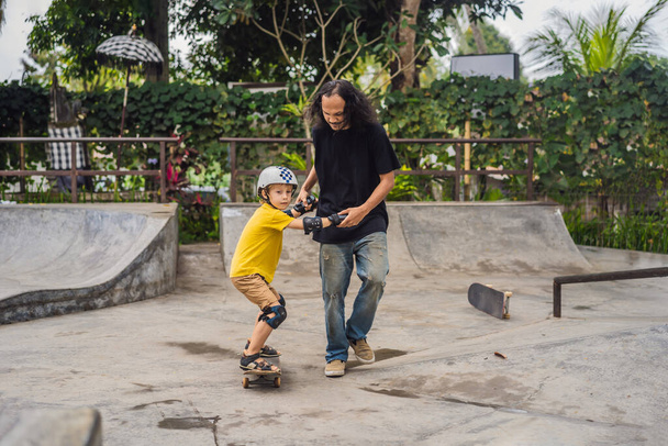 "Athletic boy learns to skateboard with a trainer in a skate park. Children education, sports" - Foto, imagen