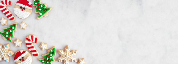 Милая граница рождественского печенья. Вид сверху на фоне белого мраморного баннера с копировальным пространством. Праздничная выпечка. Санта-Клаус, дерево, снежинки, свечи, звезды. - Фото, изображение