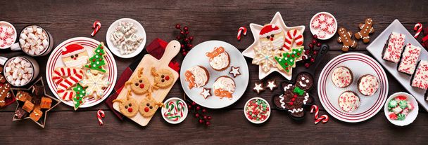 Cute Christmas sweets and cookie table scene. Top view on a rustic dark wood banner background. Fun holiday baking concept. - Photo, Image