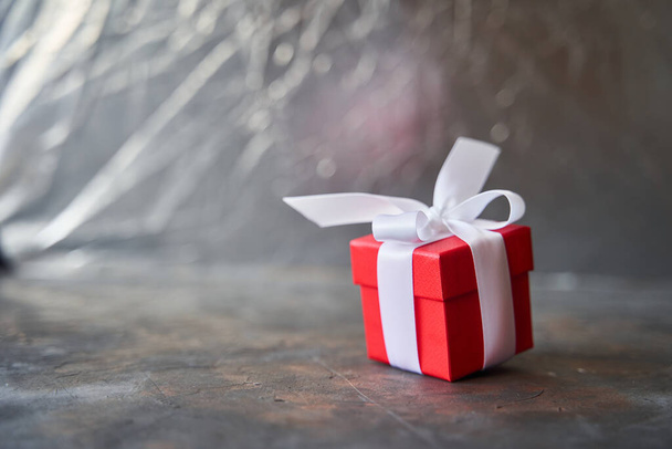 Pequeña caja de regalo roja con lazo blanco sobre fondo oscuro
 - Foto, imagen