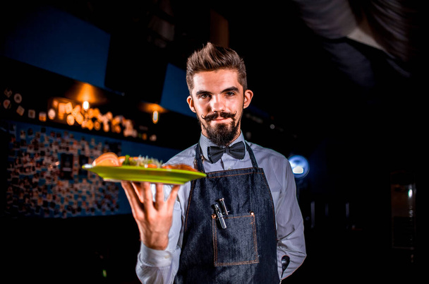 Cameriere amichevole professionale serve utilmente piatto cotto su uno sfondo nero. - Foto, immagini