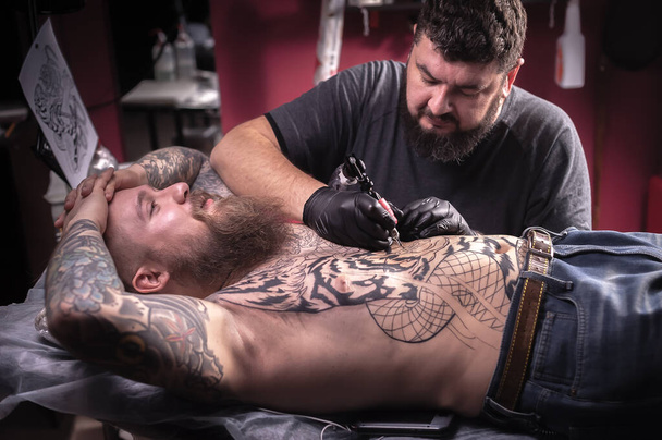 Tattooist demonstrates the process of getting tattoo in tattoo parlor - Photo, Image