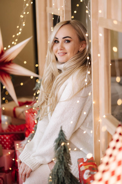Portré gyönyörű szőke hajú nő túlméretezett pulóverben nyitott ajándék karácsony idején. Elegáns nő a karácsonyfánál. Vonzó női tartás jelen. Karácsonyi hangulat. Téli szünet. - Fotó, kép