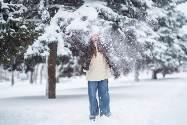Beautiful woman standing among snowy trees and enjoying first snow. Holidays, rest, travel concept. - Foto, immagini