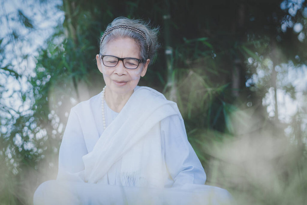 Calma di sana asiatica donna anziana in abito bianco con i capelli bianchi seduto per la meditazione di respirazione su sfondo verde natura nel parco - Foto, immagini