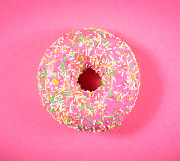 Top view of pink icing donut with sprinkles on pink background - 写真・画像