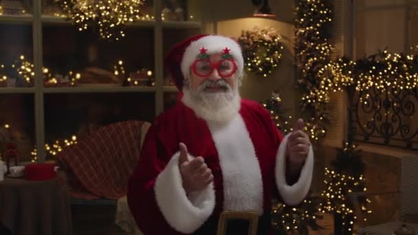 Kerstman heeft plezier buiten, in prachtige lege wintertuin, versierd met verlichting en geschenkdozen, genot van het vakantieseizoen, close-up, slow motion. - Video